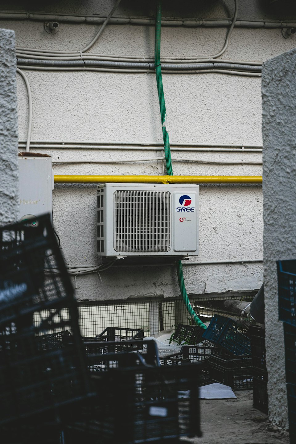Outdoor air conditioner unit mounted on a white wall with yellow pipe.