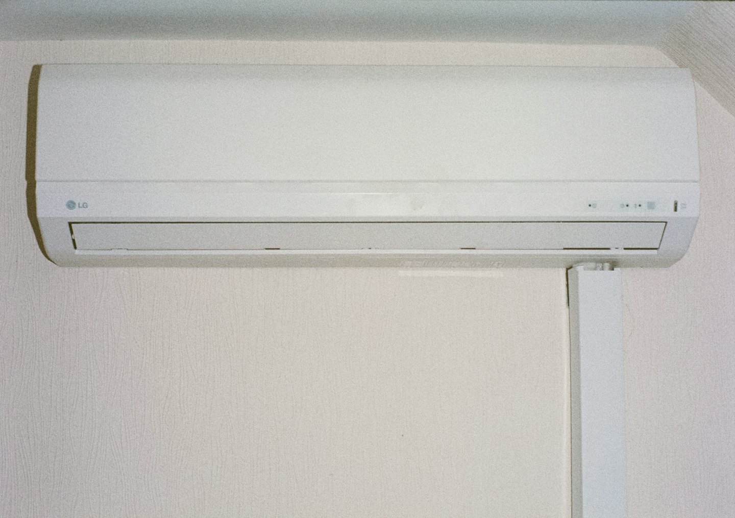 Wall-mounted air conditioner unit with white conduit on textured wallpaper.